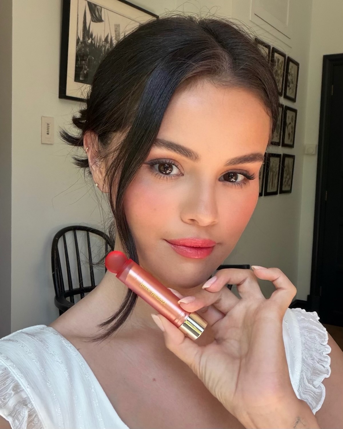 Дівчина тримає біля обличчя рожево-червоний стік Rare Beauty Soft Pinch Lip Oil Stick