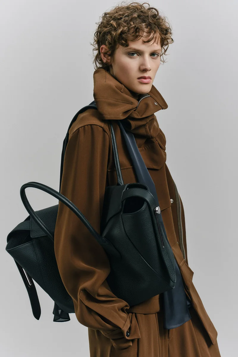 Коричневе пальто Sacai з шарфом-комірцем і чорна шкіряна сумка через плече