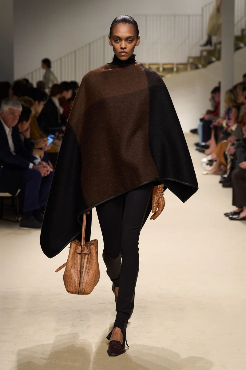 Коричнево-чорна накидка Tod's поверх чорних легінсів і руда сумка-кисет, осінь-зима 2026-2027