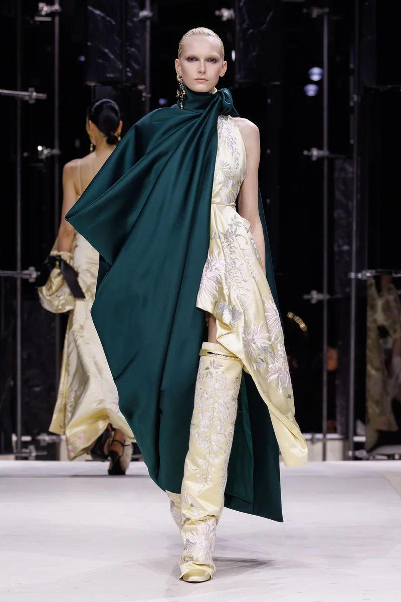 Смарагдовий атласний кейп-шарф Givenchy поверх кремової сукні з вишивкою і високі вишиті чоботи