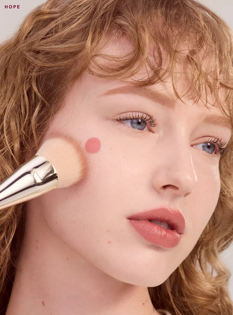 Модель із рум’янами Hope на щоці та щіткою Soft Pinch Blush Brush біля обличчя