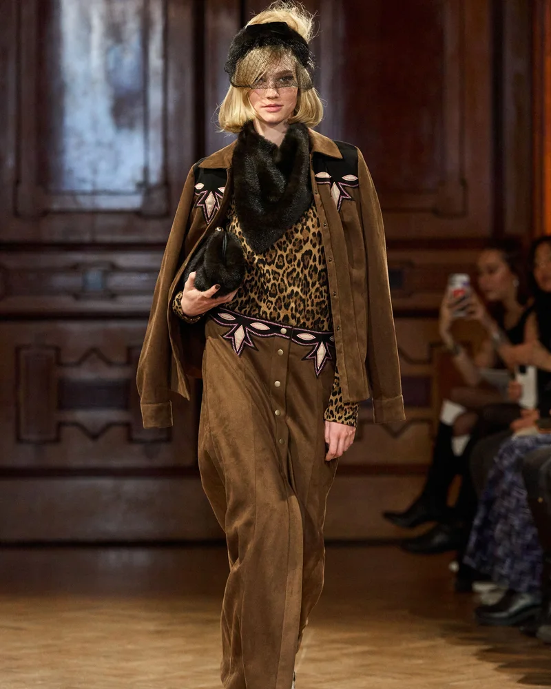 Модель Anna Sui у широкій хутряній пов'язці на голові, леопардовому топі, коричневому замшевому жакеті і хутряному шарфі