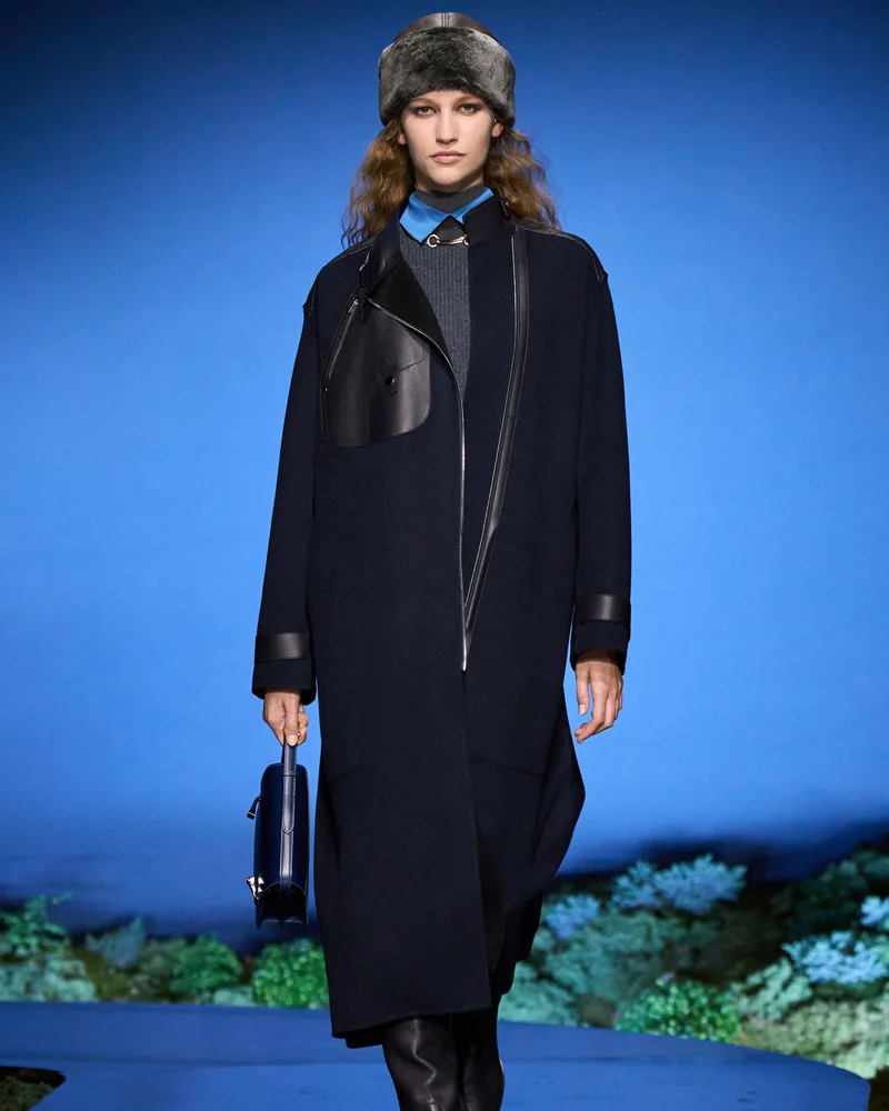 Модель Hermès у круглій сірій хутряній шапці, темно-синьому вовняному пальті з шкіряними вставками і блакитній сорочці