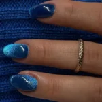 Синій манікюр котяче око на мигдалеподібних нігтях на тлі синього в'язаного светра