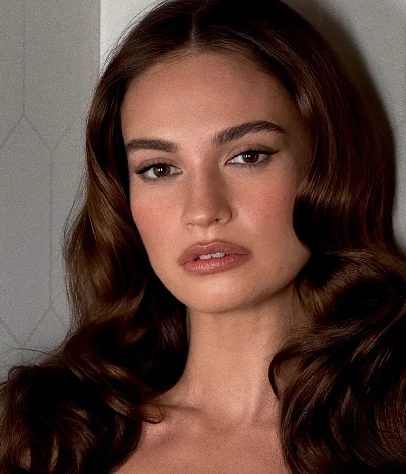 Lily James з коричневими тінями і розтушованою стрілкою, хвилясте каштанове волосся, макіяж Nina Park